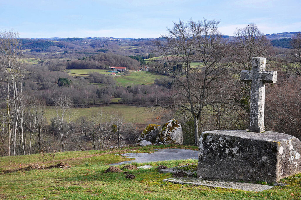 La croix du cimetière de Saint-Georges-Nigremont, les monolithes dits « le siège de César», à l'horizon le bourg de Crocq.